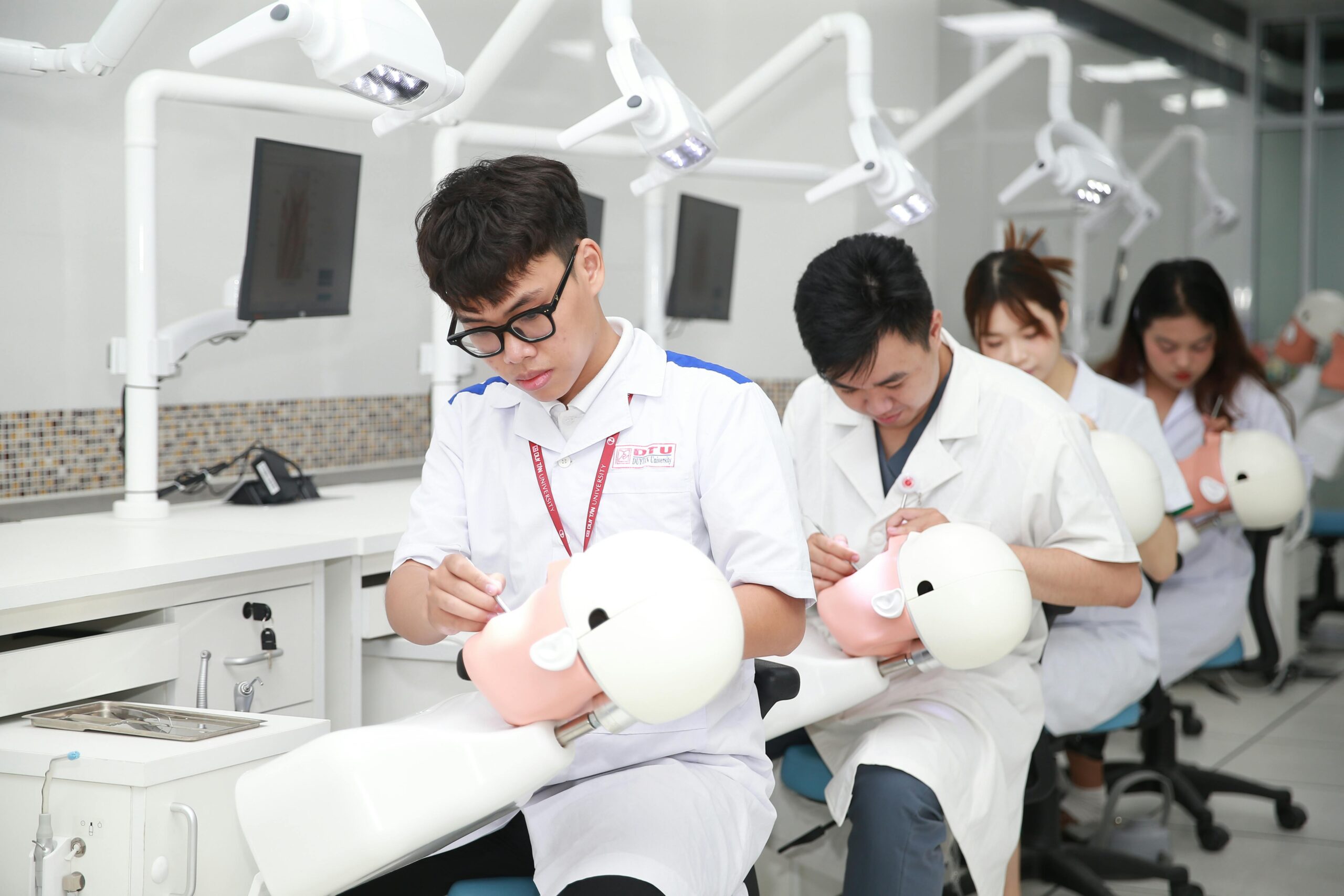 Dental students in a training lab practicing on mannequin heads for skill development.